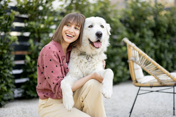 A smiling woman sits in a garden with her happy, panting dog